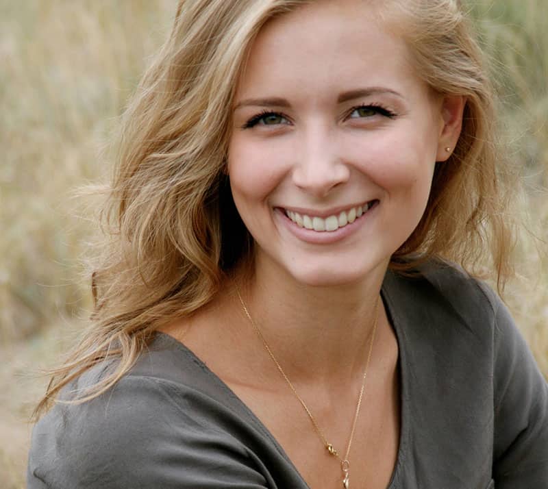 Viso di donna sorridente con capelli biondi in un ambiente naturale.