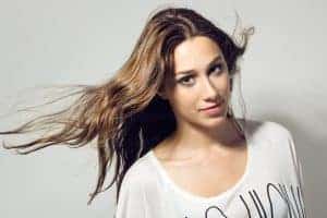 Donna con capelli mossi e sorriso naturale, indossa una maglietta bianca, sfondo neutro.