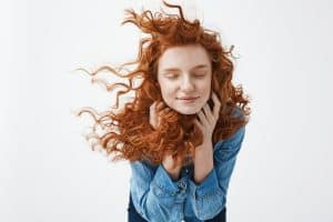 Pelle morbida e capelli ricci mossi al vento, donna con espressione serena e capelli rossi.