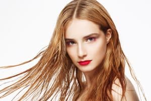 Donna con capelli lunghi e mossi, colore rosso, che guarda in camera con sfondo bianco.