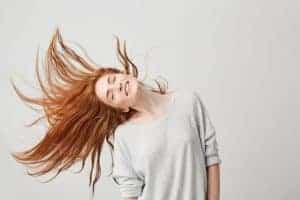 Donna con capelli lunghi e mossi che si muovono, sorriso felice, abbigliamento casual grigio.