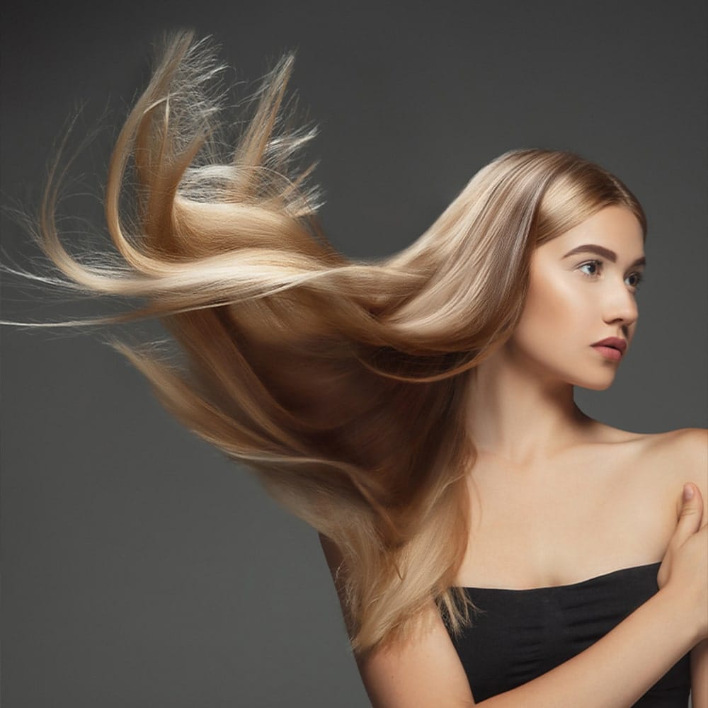 Lunghe ciocche di capelli lisci e lucenti di una donna con sfondo grigio scuro.