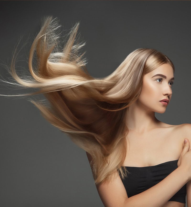 Lunghe ciocche di capelli lisci e lucenti di una donna con sfondo grigio.