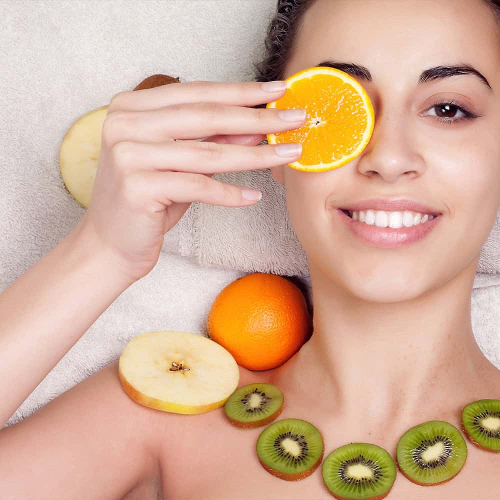 Frau con frutta fresca e arancia, promuovendo salute e bellezza naturale.