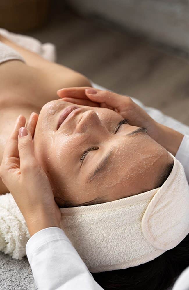Trattamento di massaggio viso rilassante su donna con asciugamano e crema.