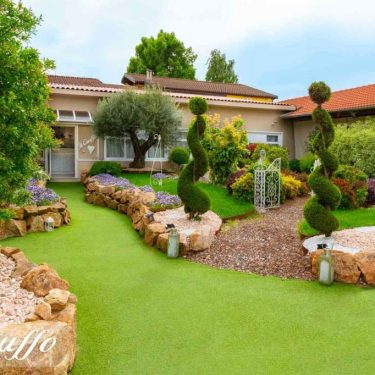 Giardino con piante e aiuole ben curate, decorato con arbusti sagomati e pietre decorative.