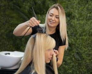 Taglio capelli donna all'aperto, parrucchiera che lavora con cliente.